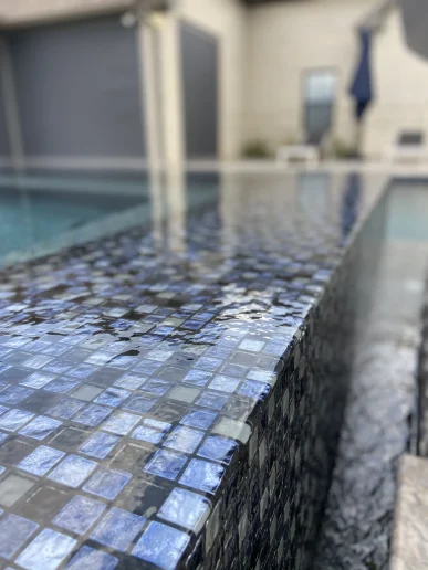 Close-up of glass tile pool waterline and edge detail with flowing water
